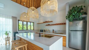 A modern kitchen with a large island, stainless steel appliances, wicker chairs, and a ceiling with geometric light fixtures. - Villa Air - 2BR Villa in Pererenan (Canggu)
