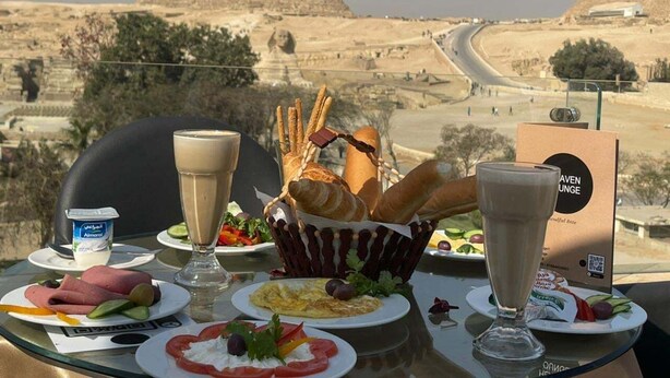 A table with food and drinks, overlooking a desert landscape with pyramids. - Thomas Cook pyramids  guest house (Giza)