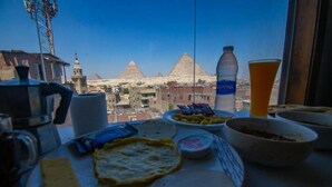 A table with food items and a water bottle, with a view of pyramids in the background. - Thomas Cook pyramids  guest house (Giza)