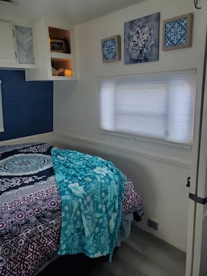 Un dormitorio con cama, ventana con persianas, armario y adornos en la pared.