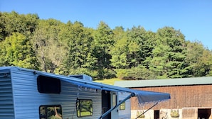 Una casa móvil con un patio, una zona de estar cubierta al aire libre y un granero al fondo.