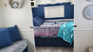 Un dormitorio pequeño con cama, una zona de descanso y un armario blanco con objetos decorativos.