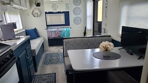 Una cocina compacta con estufa, fregadero y una zona de comedor con mesa y banco.