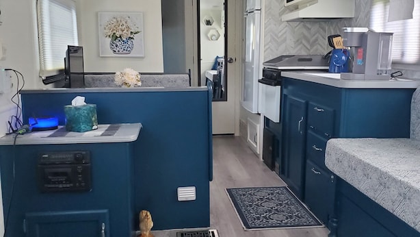 Una cocina compacta con detalles azules, microondas, cafetera y refrigerador.