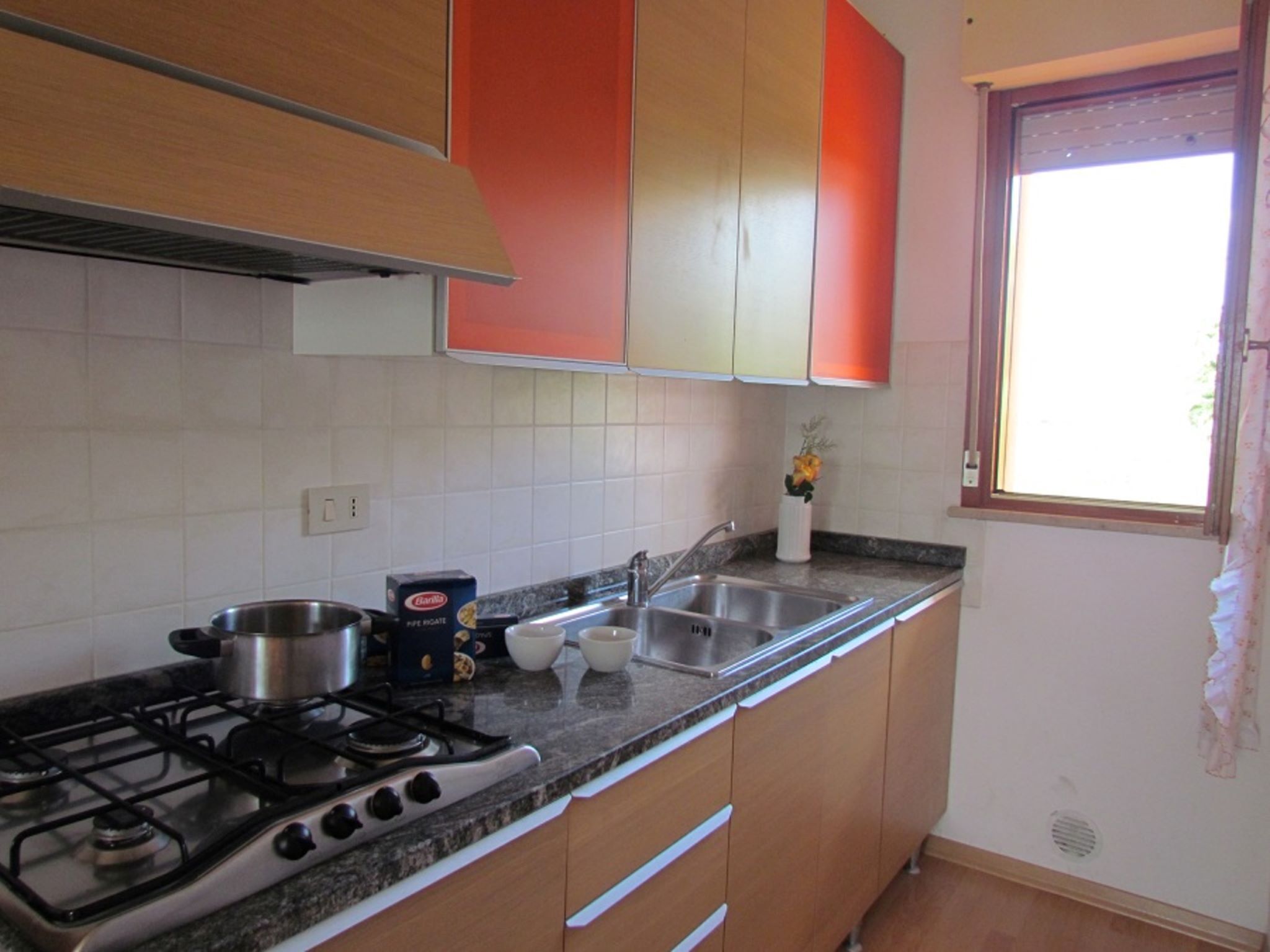 Een keuken met een gasfornuis, een roestvrijstalen spoelbak en houten kastjes.