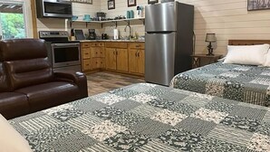 A cozy room with a bed, a chair, a kitchenette, and a refrigerator. - PineyWoods House Forest Retreat (Bastrop County)