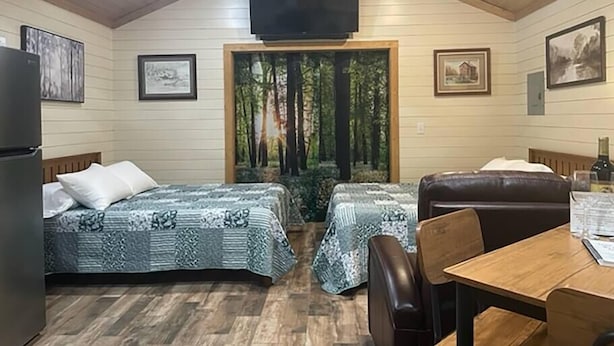 A room with two beds, a ceiling fan, a TV, and a dining table with chairs. - PineyWoods House Forest Retreat (Bastrop County)