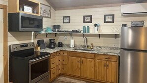 A kitchen with wooden cabinets, a stainless steel refrigerator, a microwave, and a coffee maker. - PineyWoods House Forest Retreat (Bastrop County)