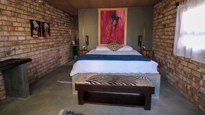 Ein Schlafzimmer mit Backsteinwand, einem Bett mit einer Sitzbank im Zebra-Muster und einem großen Gemälde darüber.