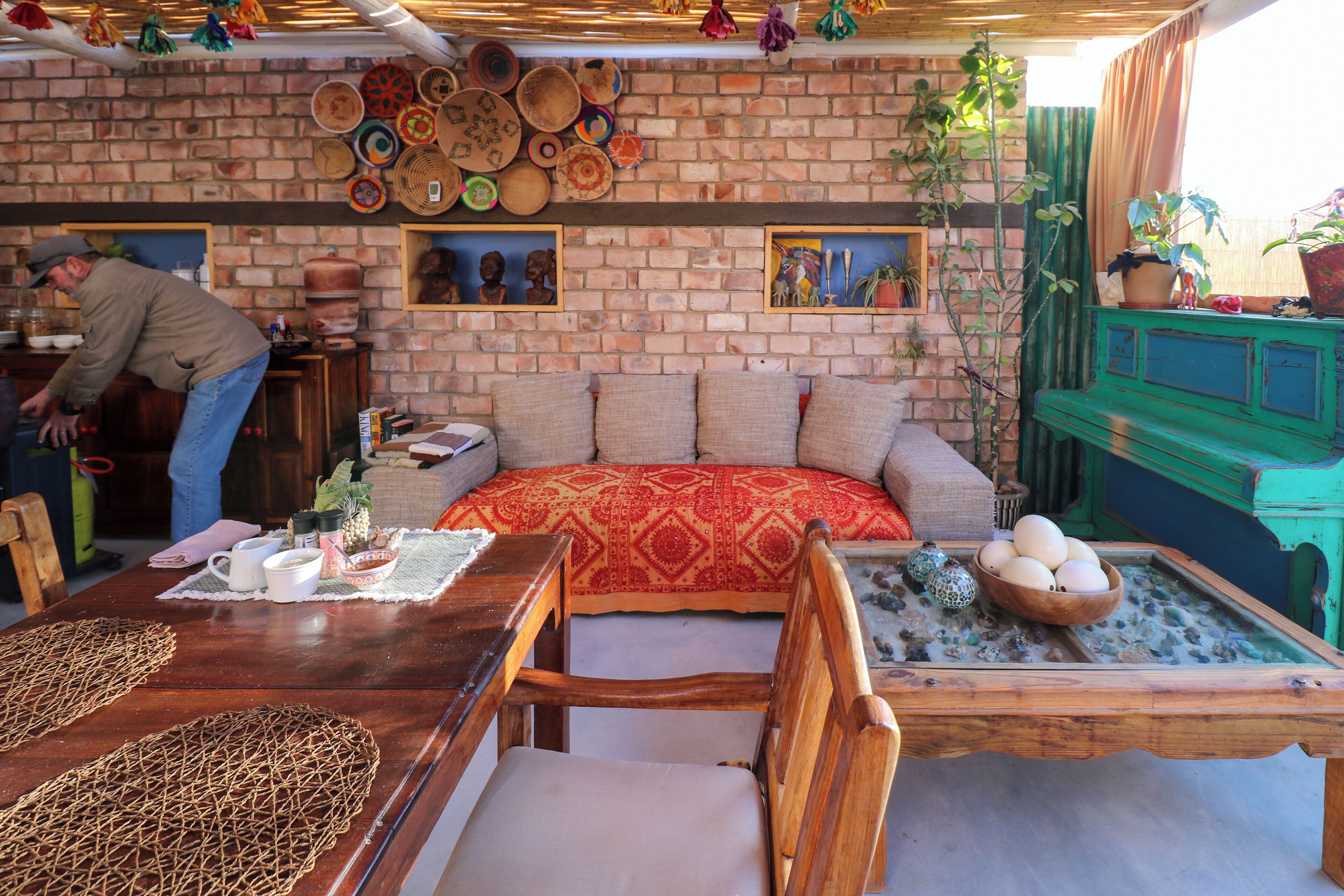A cozy room with a brick wall, a sofa with patterned cushions, a wooden dining table with a placemat, and a green cabinet.