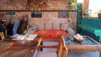 A cozy room with a brick wall, a sofa with patterned cushions, a wooden dining table with a placemat, and a green cabinet.