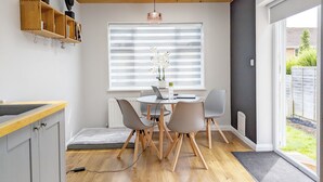 A modern kitchen with a wooden ceiling, a dining area with a table and chairs, and a window with blinds.