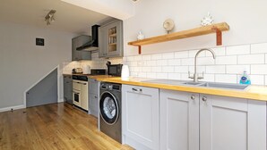 A compact kitchen with grey cabinets, a wooden countertop, a built-in washing machine, and a sink.