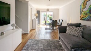 A modern living room with a grey sofa, a flat-screen TV, and a dining area with a table and chairs.