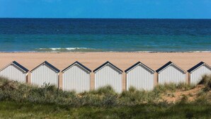 A beach with a row of white beach huts and the ocean in the background. - Entire Seaside House, 160m² – 3 Bedrooms, Sleeps 6 (Ouistreham)
