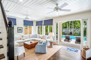 A spacious living room with a sectional sofa, a coffee table, and a blue accent chair. There is a large window with a view of a pool and greenery. - ~SANCTUARY ON SOUTH~ A pool, privacy and posh design abound! (Key West)