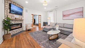 Ein modernes Wohnzimmer mit Kamin aus Stein, einem Flachbildfernseher, einem grauen Sofa und einem großen Gemälde.