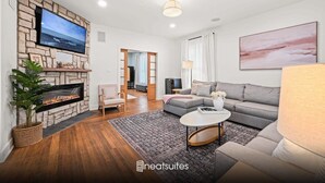 A modern living room with a stone fireplace, a flat-screen TV, a grey sofa, and a large window with curtains.