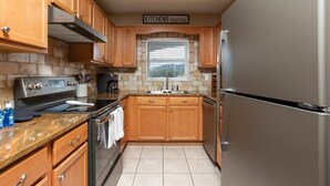 A compact kitchen with wooden cabinets, a stainless steel refrigerator, a built-in oven, and a granite countertop. - On River/Mt. LeConte Views/DwTn (Pigeon Forge)