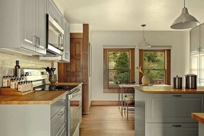 Une cuisine moderne avec des meubles blancs, un plan de travail en bois et une vue sur la verdure par une fenêtre.