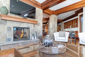 Amplia sala de estar con chimenea de piedra, vigas de madera y una cocina moderna al fondo.