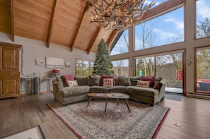 A spacious living room with a large sectional sofa, a wooden ceiling, and a Christmas tree.