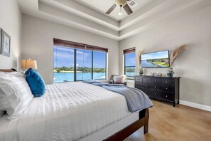 A bedroom with a large bed, a TV, a dresser, and a view of a body of water.