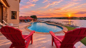 A swimming pool with a sunset view, red chairs, and a dock extending into the water. - 119 Christopher | Concierge Services Available (Kingsland)