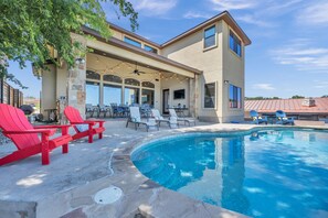 A pool area with red Adirondack chairs, a covered patio, and a stone building with large windows.
