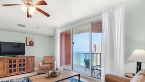 Uma sala de estar espaçosa com uma grande televisão de tela plana, uma mesa de centro de madeira, um sofá e uma varanda com vista para o oceano.
