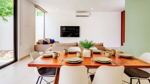 Uma sala de jantar moderna com uma mesa de madeira posta para quatro pessoas, rodeada por cadeiras brancas.