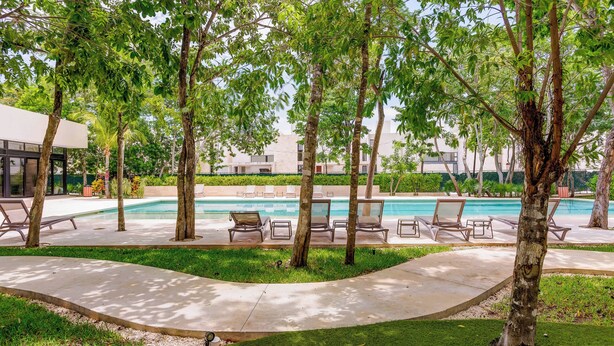 Uma área junto à piscina com espreguiçadeiras e piscina, cercada por árvores e um edifício ao fundo.