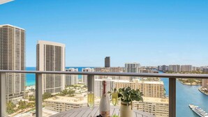 A balcony with a wooden table, a bottle of wine, a glass, and a bowl of grapes. - Luxury Hollywood Beach 3BR|Ocean View (Hollywood)