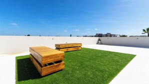 Une terrasse sur le toit, avec un revêtement d’herbe artificielle et des meubles en bois.