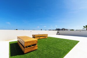 A rooftop terrace with artificial grass and wooden furniture. - Rooftop Terrace Views: 2BR Condo w/ Pool (Noord)
