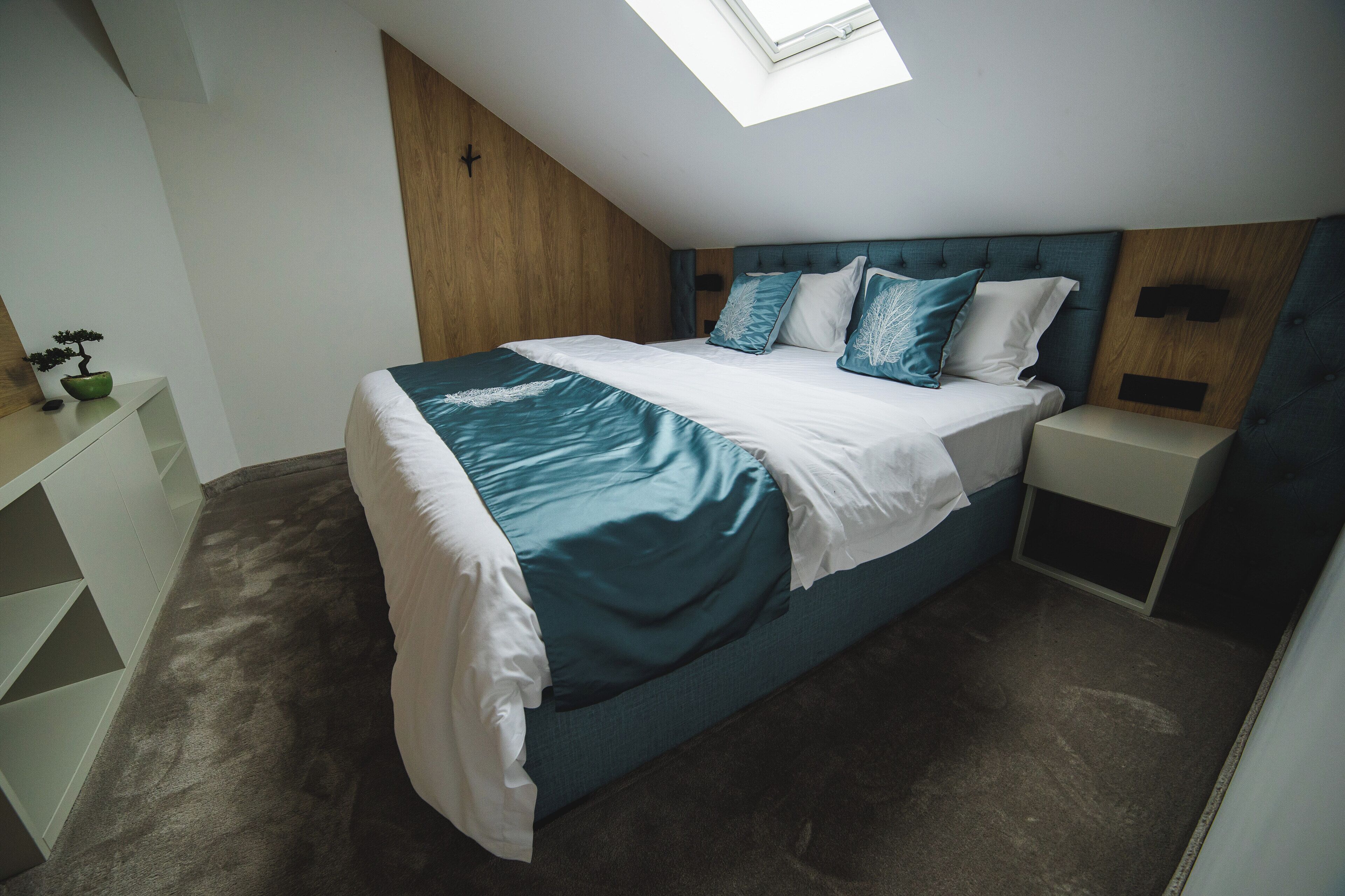 A modern bedroom with a skylight, a bed with teal and white bedding, and a wooden accent wall.