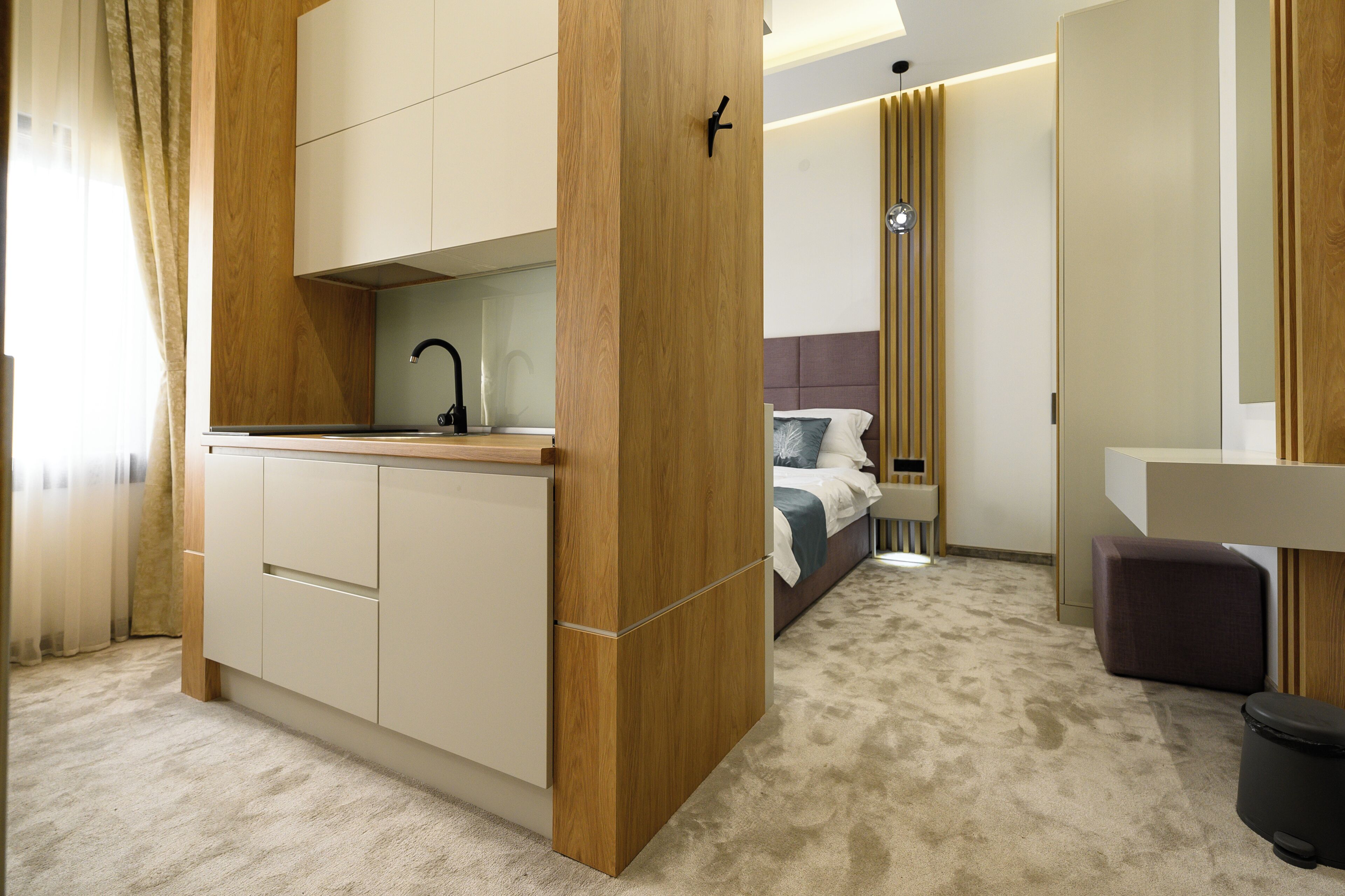 Una habitación de hotel moderna con kitchenette, una cama con cabecera y un baño con espejo.