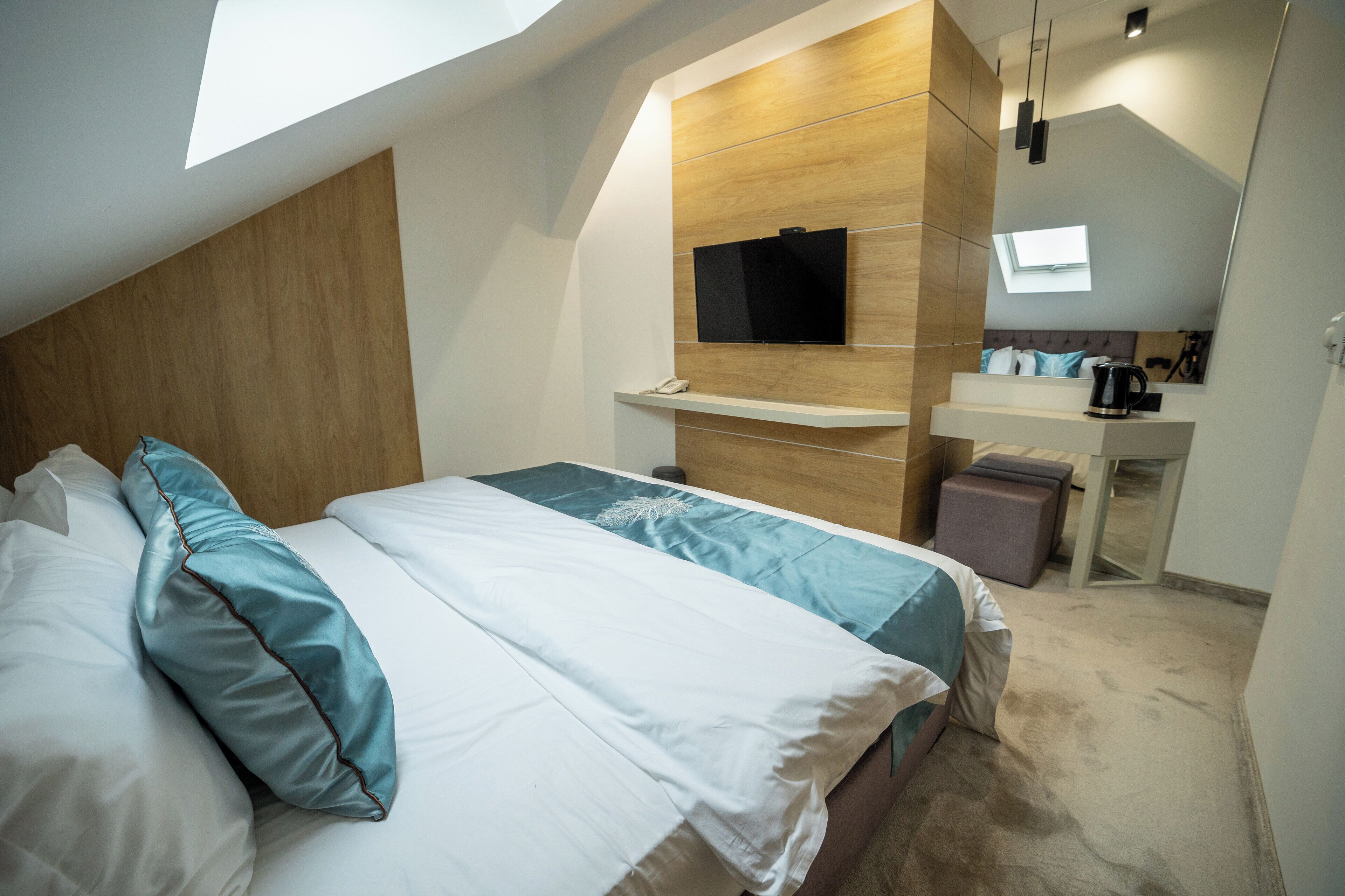 Een moderne slaapkamer met een bed, een wandtelevisie, een bureau met stoel en een klein raam.