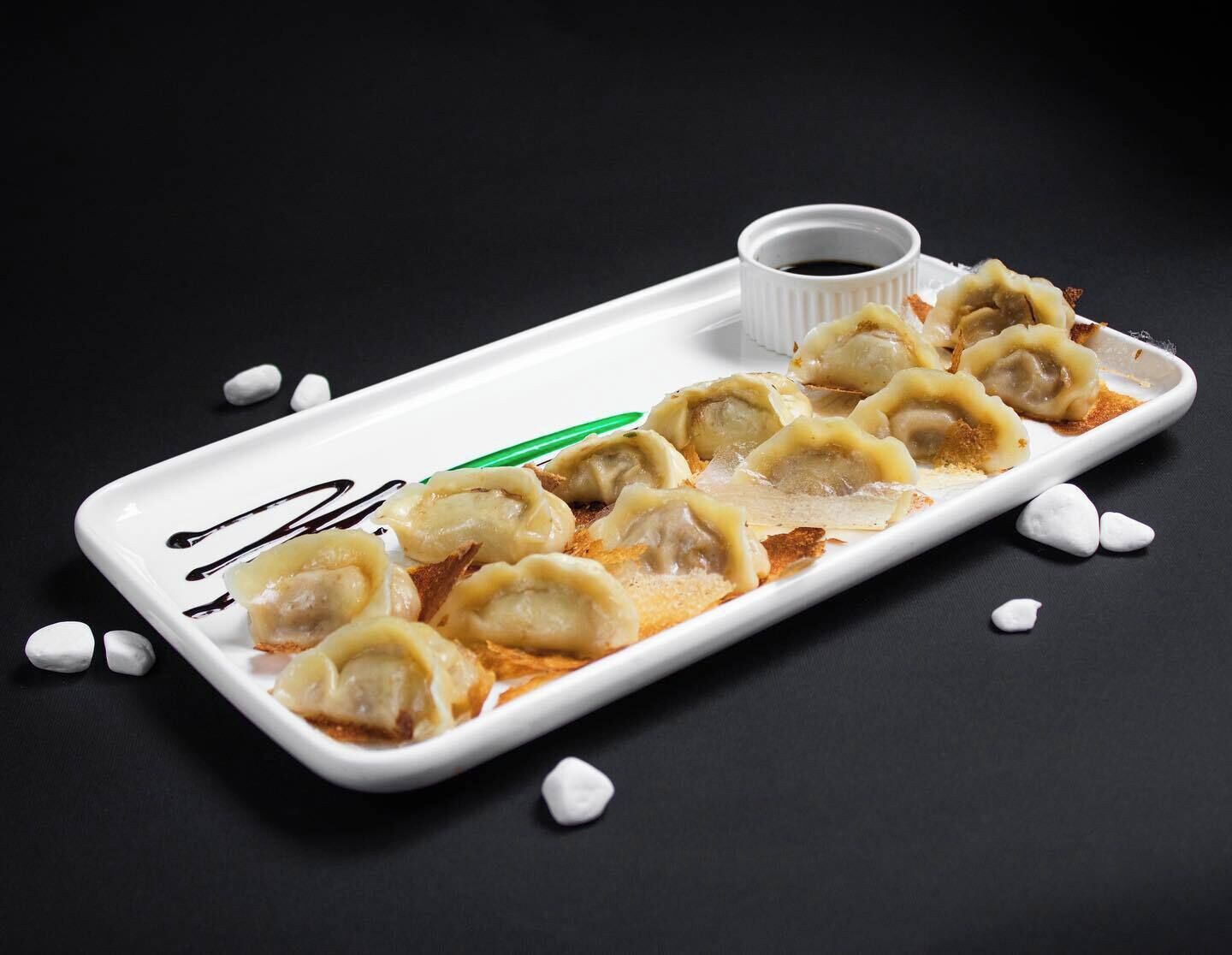 A white rectangular plate with dumplings and a small bowl of sauce, set against a dark background.