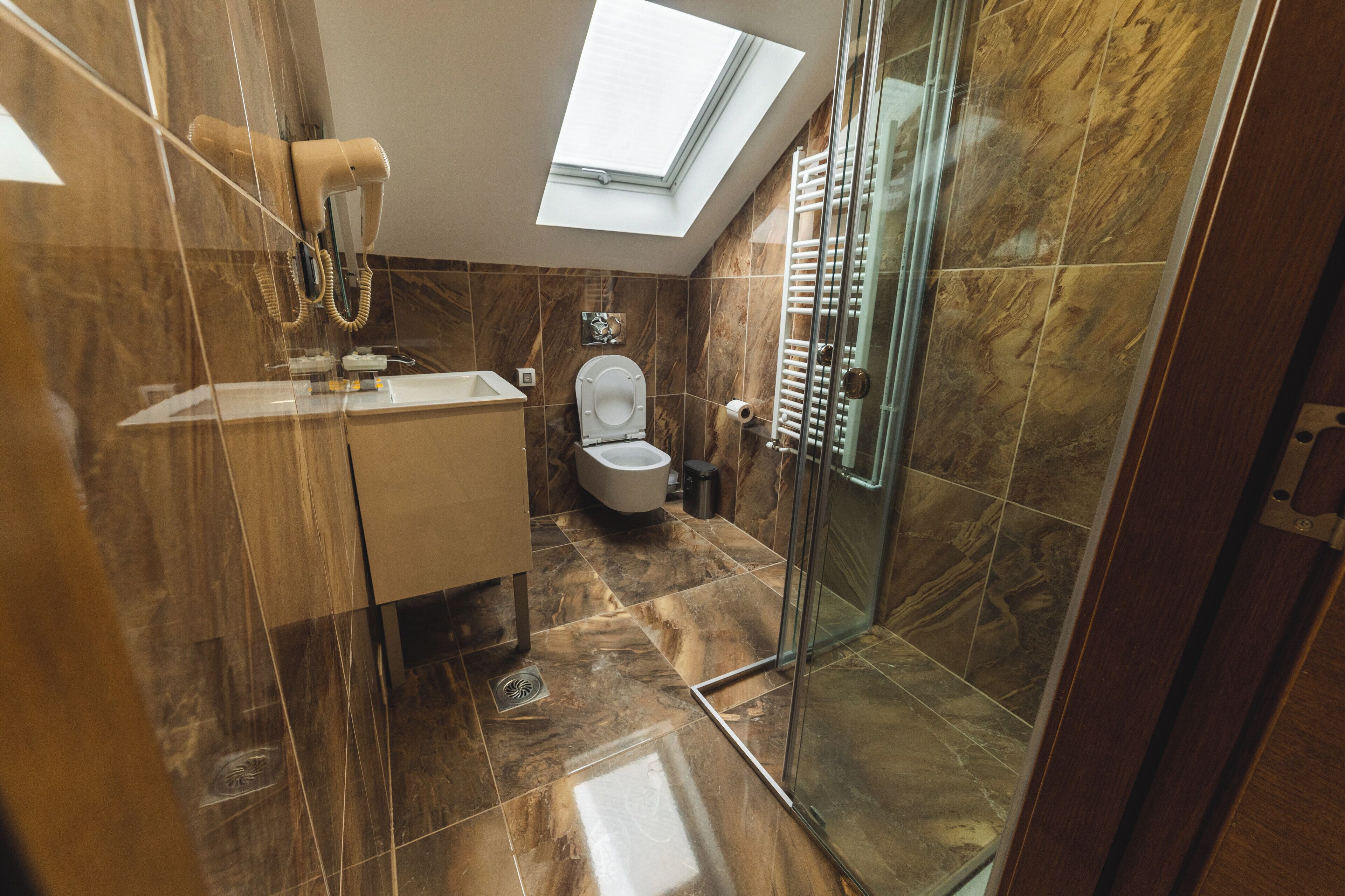 A modern bathroom with a skylight, a glass shower enclosure, and a marble-tiled floor.