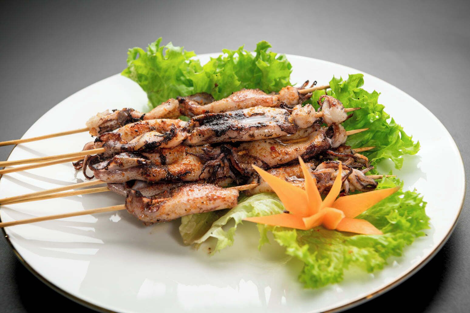 Een bord gegrilde spiezen met sla en een decoratieve wortel.