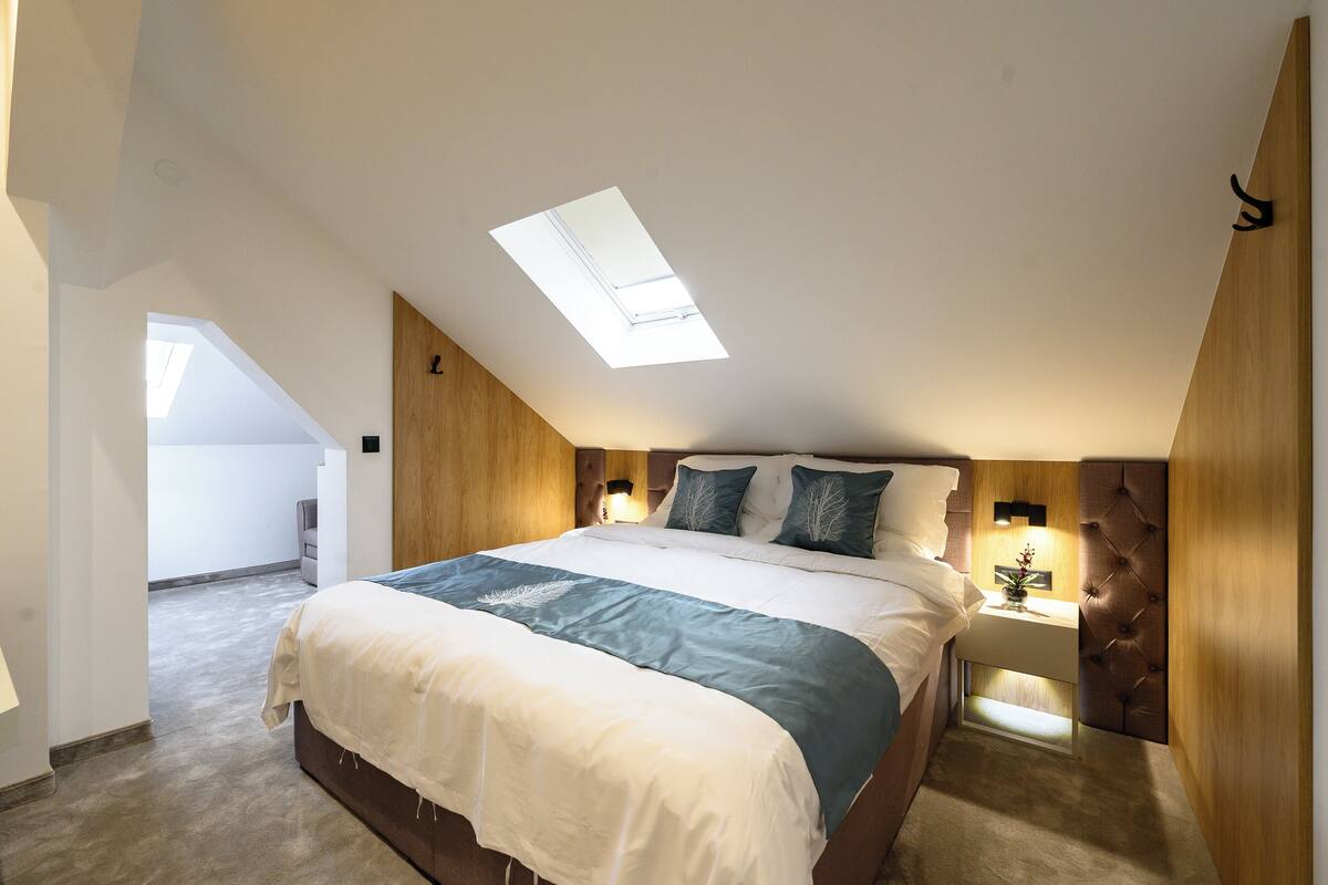 A bedroom with a skylight, a bed with a blue and white bedspread, a nightstand with a lamp, and a wooden headboard.