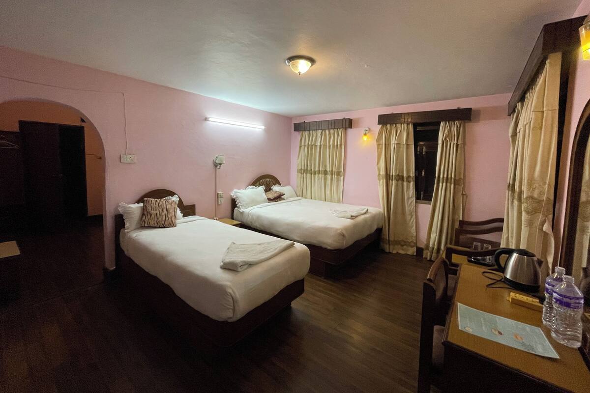 A hotel room with two beds, a desk with a kettle, and a chair.