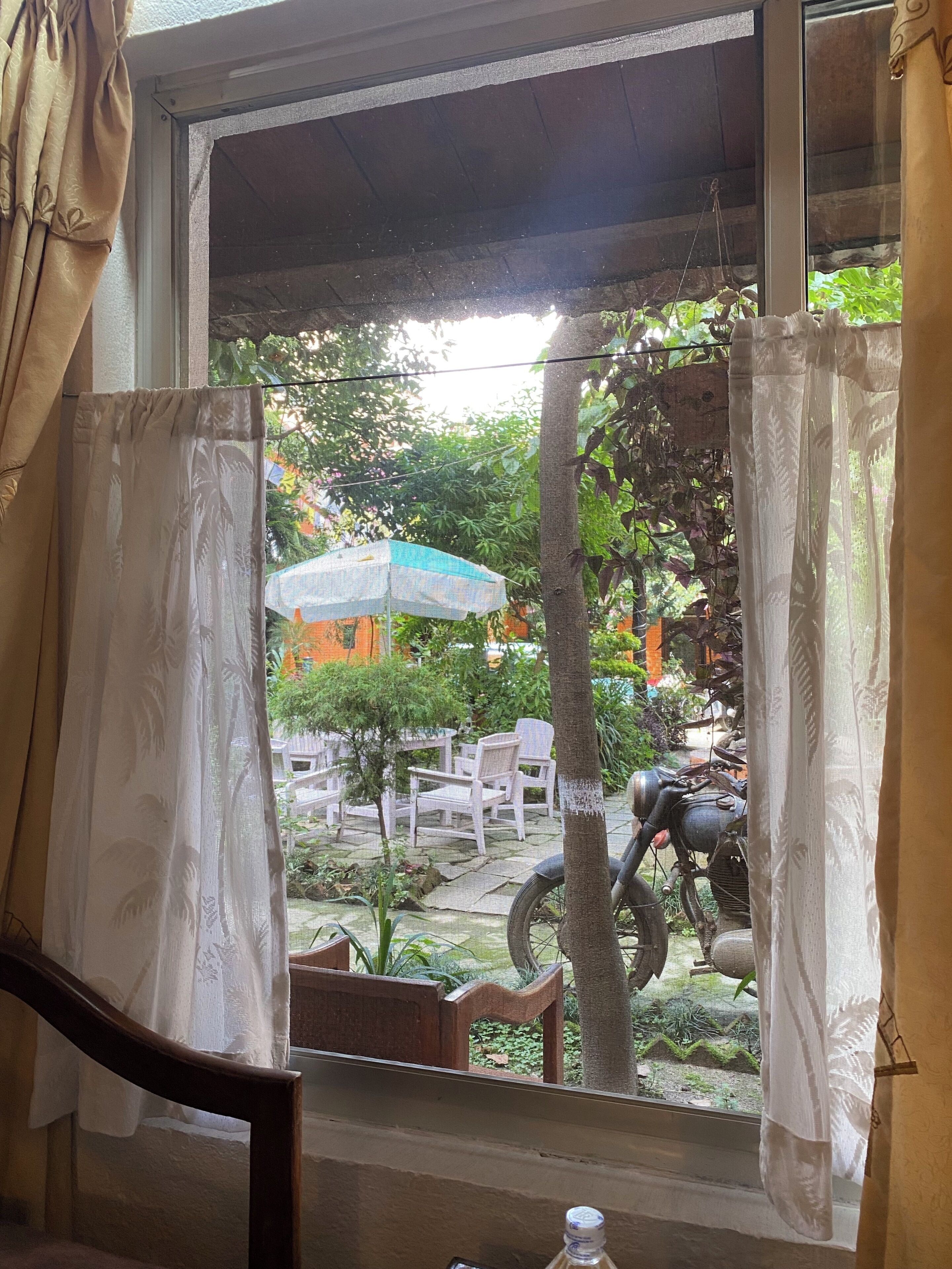 A window with a view of an outdoor seating area, including chairs and a motorcycle.