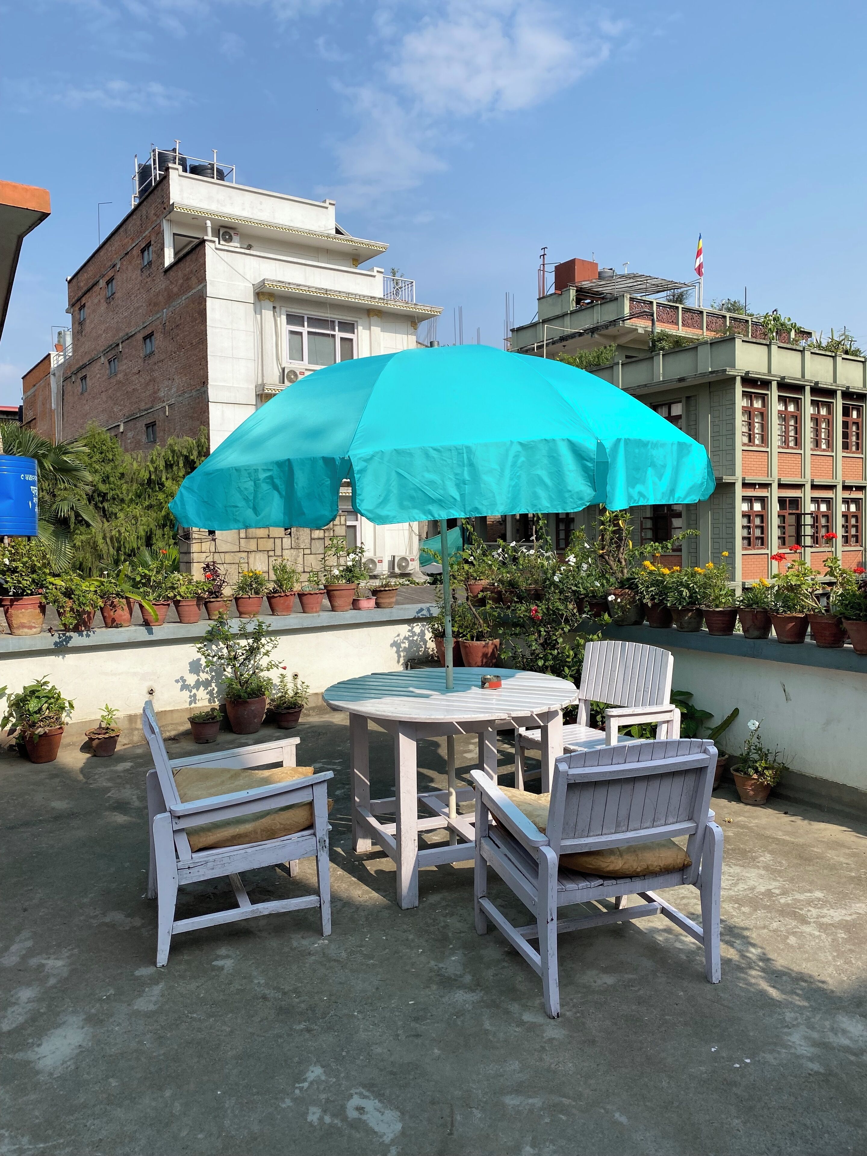A rooftop patio with a round table and two chairs, surrounded by potted plants.