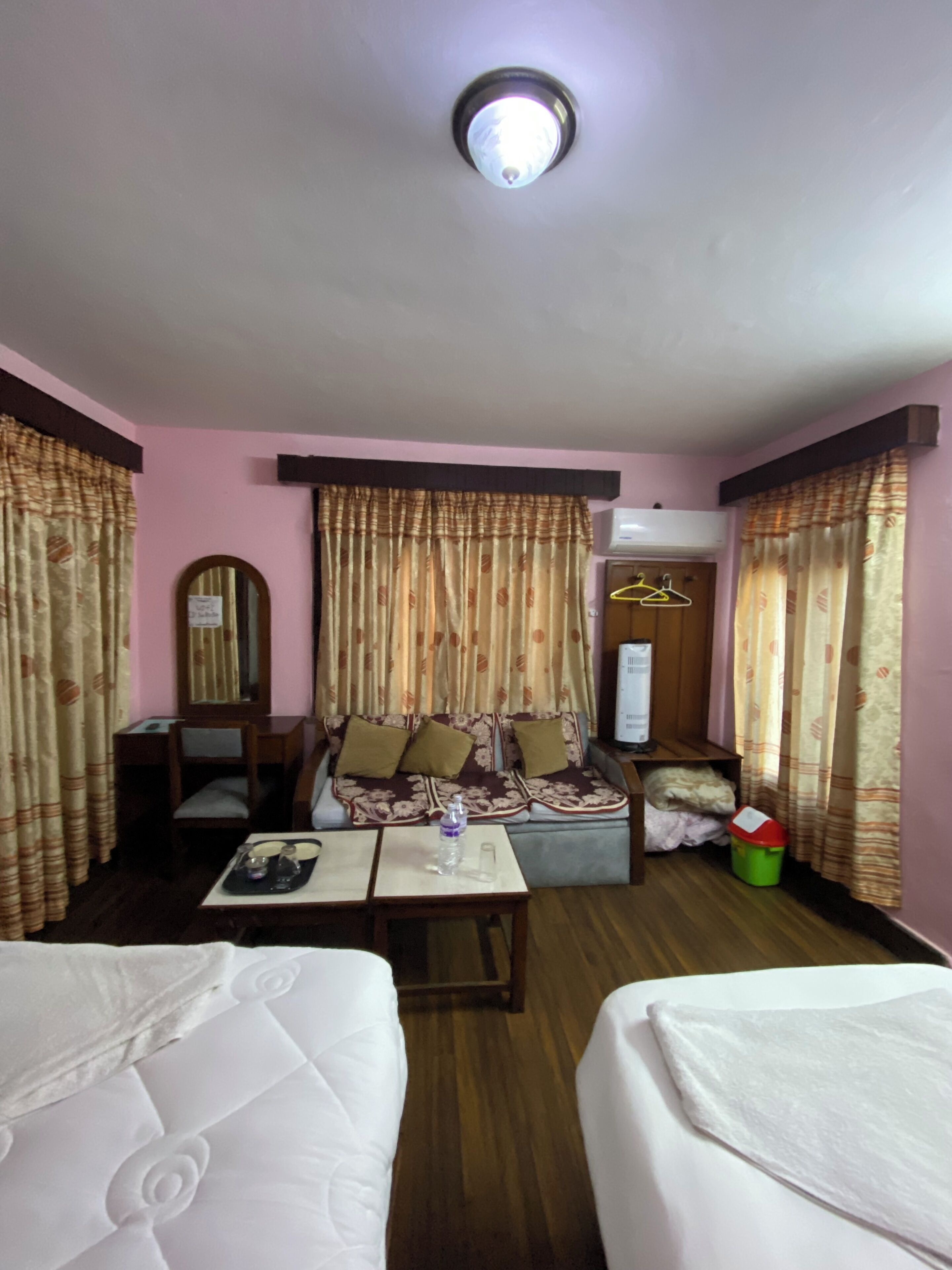 Quarto de hotel com duas camas, um sofá, uma mesa com bandeja, um espelho e cortinas.