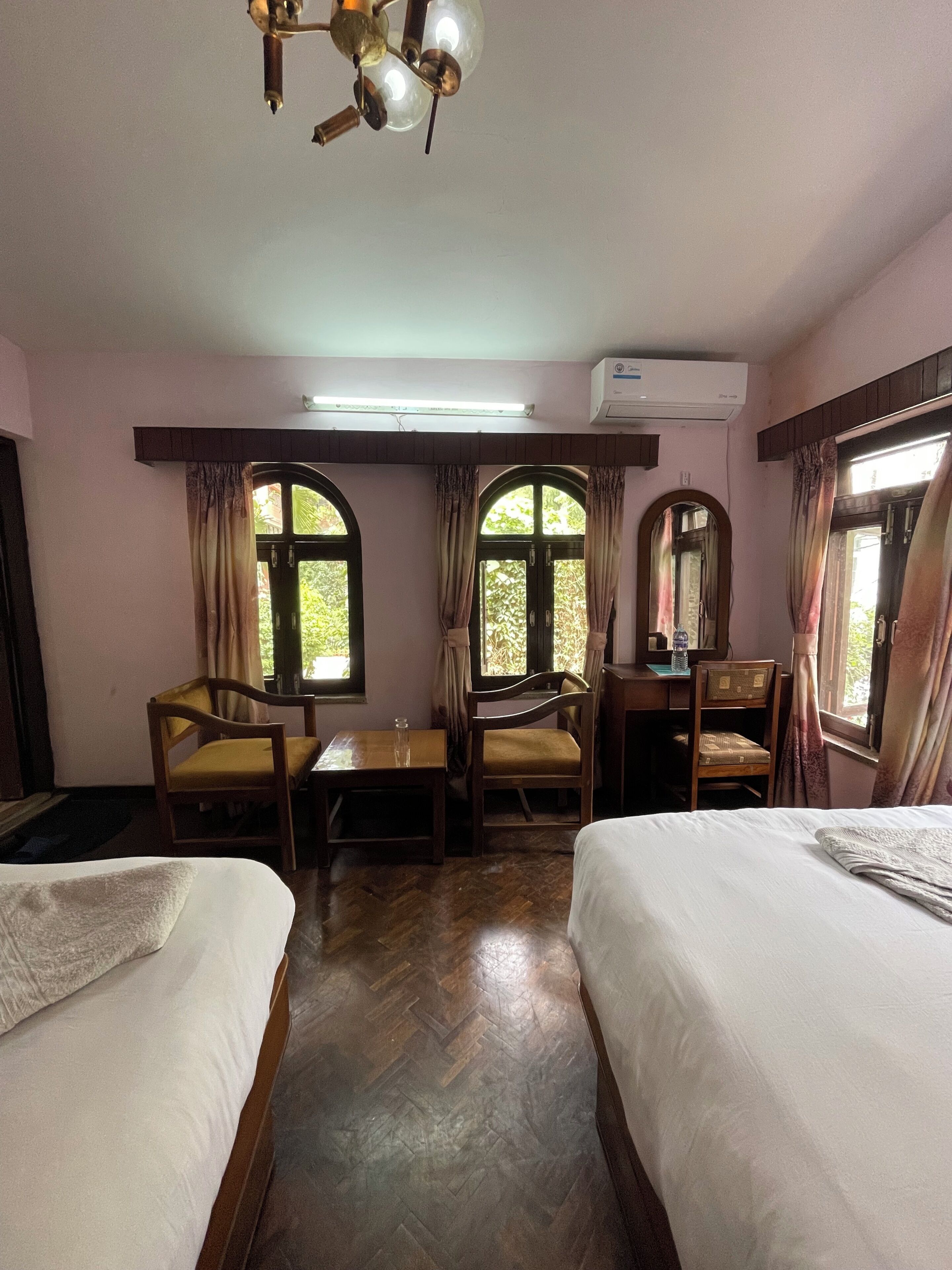 Una habitación de hotel con dos camas, un escritorio, una silla y un ventilador de techo.