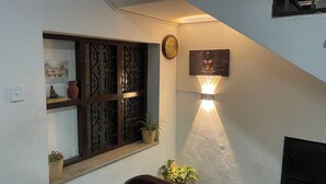 A staircase with a handrail, a wall-mounted light fixture, a clock, and a window with decorative metal grilles. - Sunrise Cottage (Kathmandu)