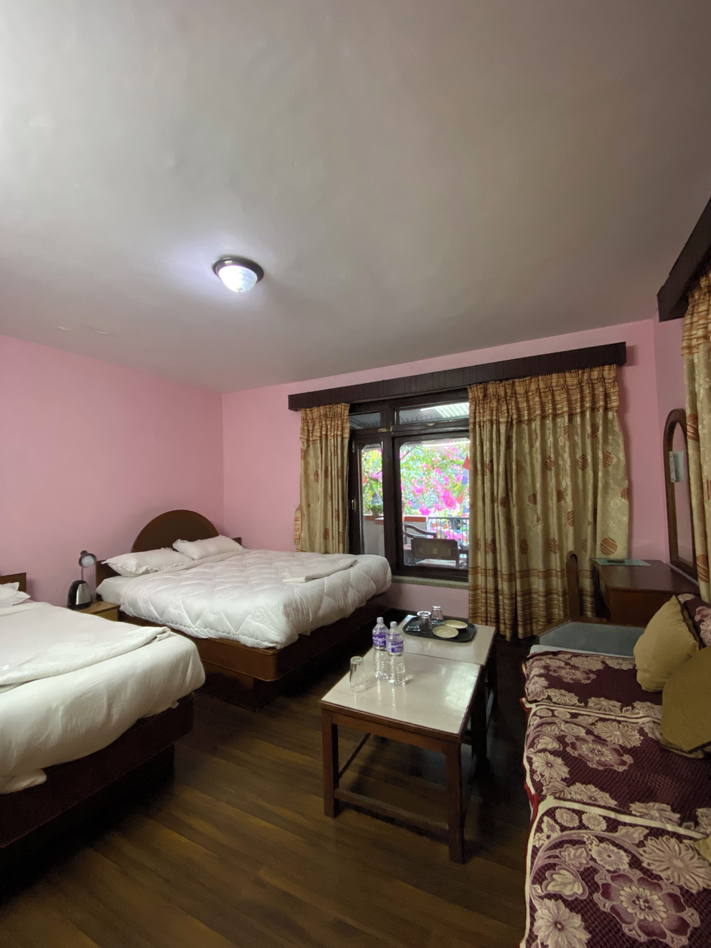 A hotel room with two single beds, a wooden table with a tray, a sofa, and a window with curtains.