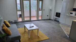 Moderni olohuone, jossa on harmaa sohva, keltaiset koristetyynyt, pieni pöytä ja kaukosäädin.